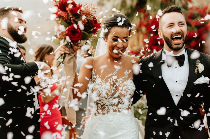 Happy newlyweds walk through white confetti with large smiles on their faces